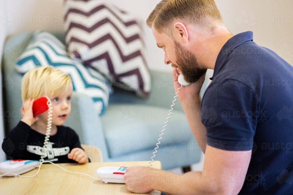 Father and son talking on toy phone - Australian Stock Image