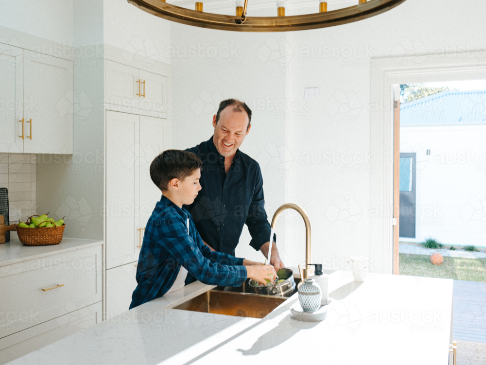 Father and son washing apples in the kitchen sink. - Australian Stock Image