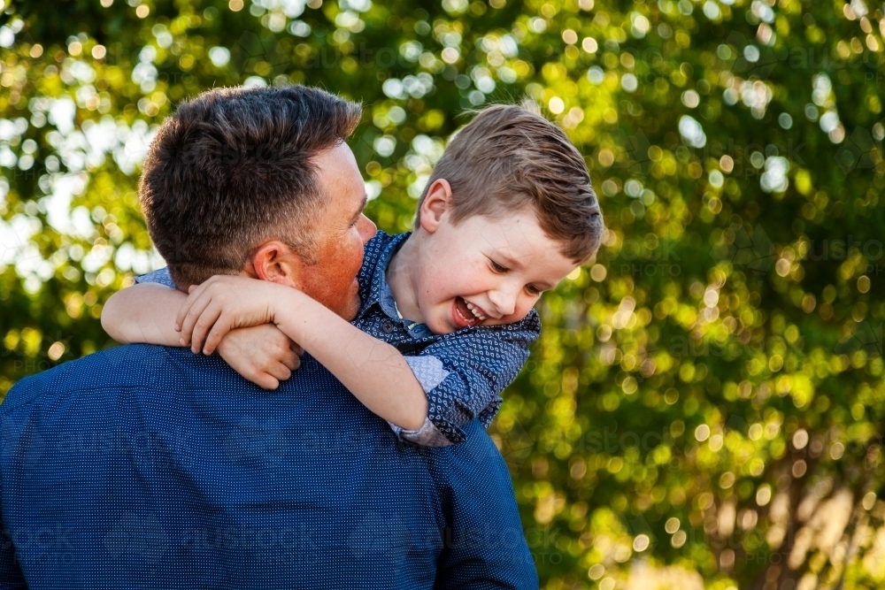 Father and young son laugh together and hug outside - Australian Stock Image
