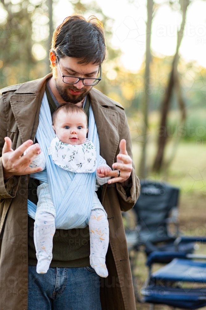 Father babywearing infant in wrap carrier at campsite - Australian Stock Image