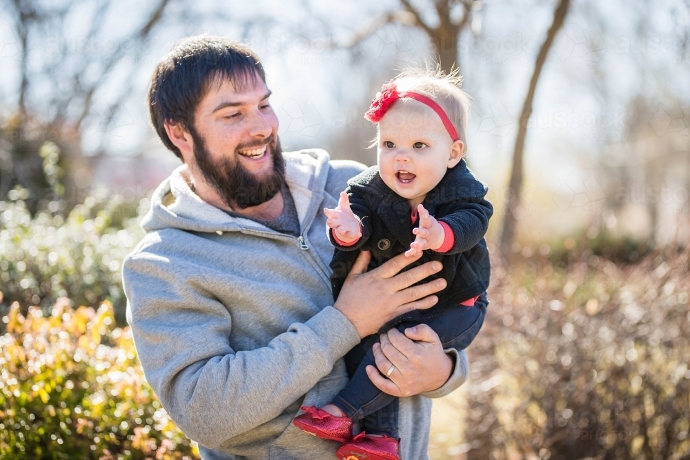 Father holding child on hip laughing at child reaching - Australian Stock Image