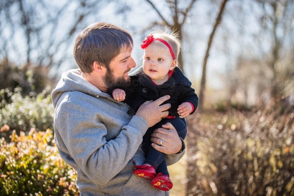 Father holding daughter close standing outside in garden - Australian Stock Image