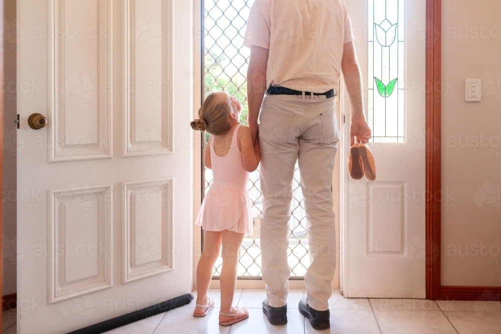 Father holding daughter's hand walking out front door of home to ballet lesson - Australian Stock Image