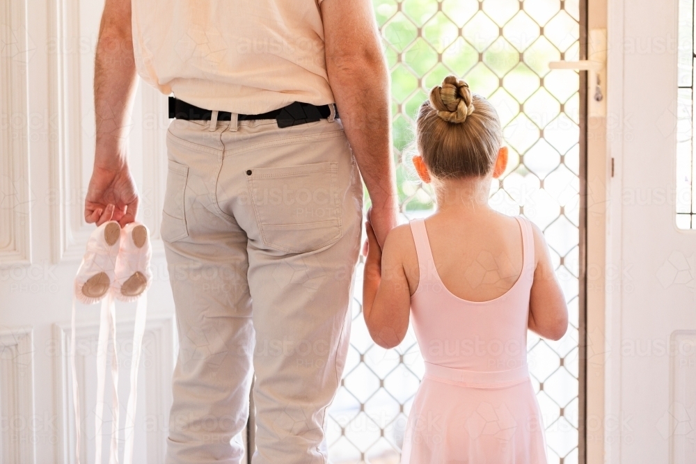 Father holding daughter's hand walking out front door of home to ballet lesson - Australian Stock Image