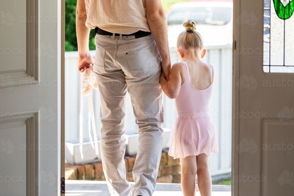 Father holding daughter's hand walking out front door to ballet lesson - Australian Stock Image