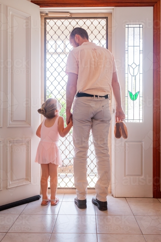 Father holding daughter's hand walking out front door to ballet lesson together - Australian Stock Image