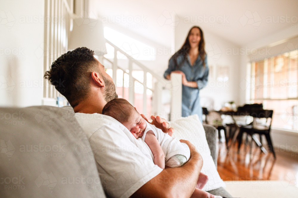 Father holding newborn baby while sitting on the couch - Australian Stock Image