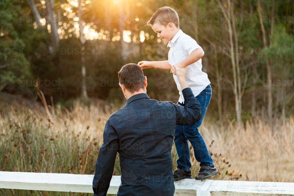 Father holding son's hand helping him balance on fence - Australian Stock Image