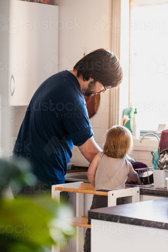 Father in kitchen with daughter teaching her how to wash dishes - Australian Stock Image