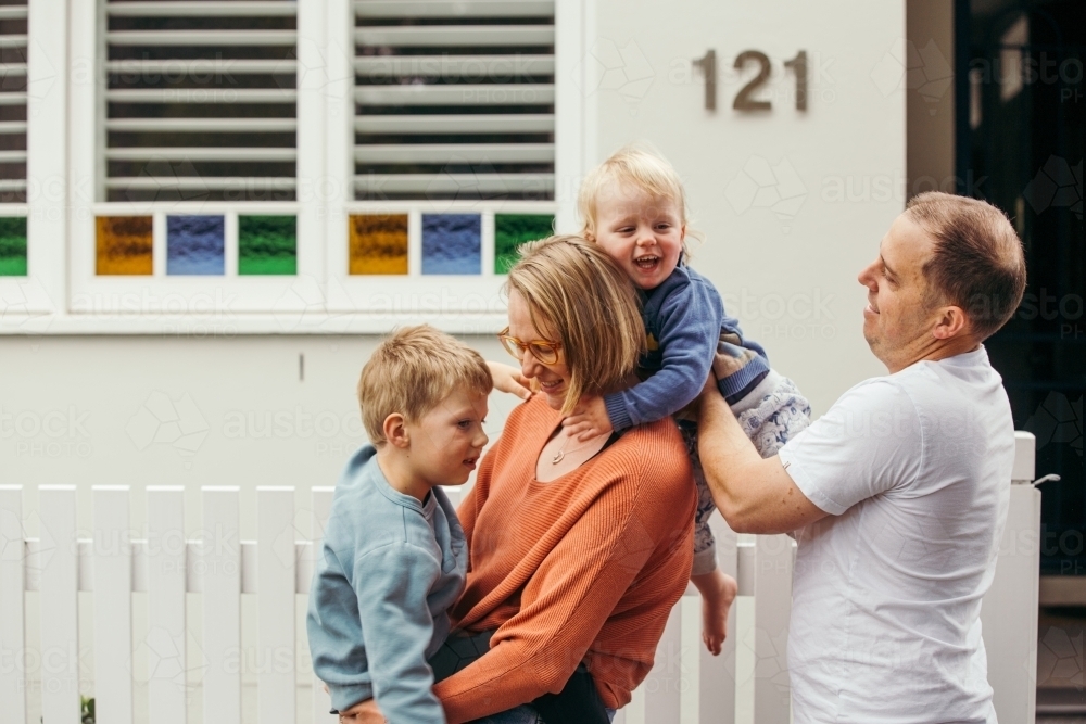 Father putting a toddler on his wife's back as she holds her preschooler son - Australian Stock Image