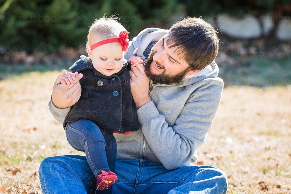 Father sitting on ground talking to baby daughter - Australian Stock Image