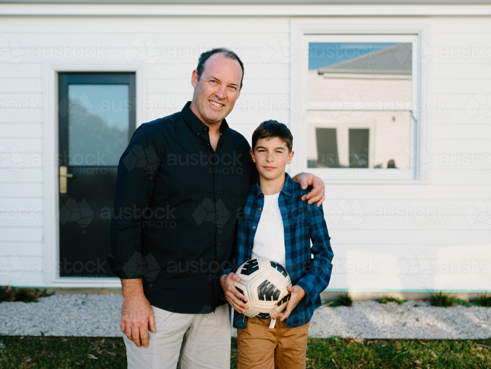 Father standing beside his son holding a soccer ball. - Australian Stock Image