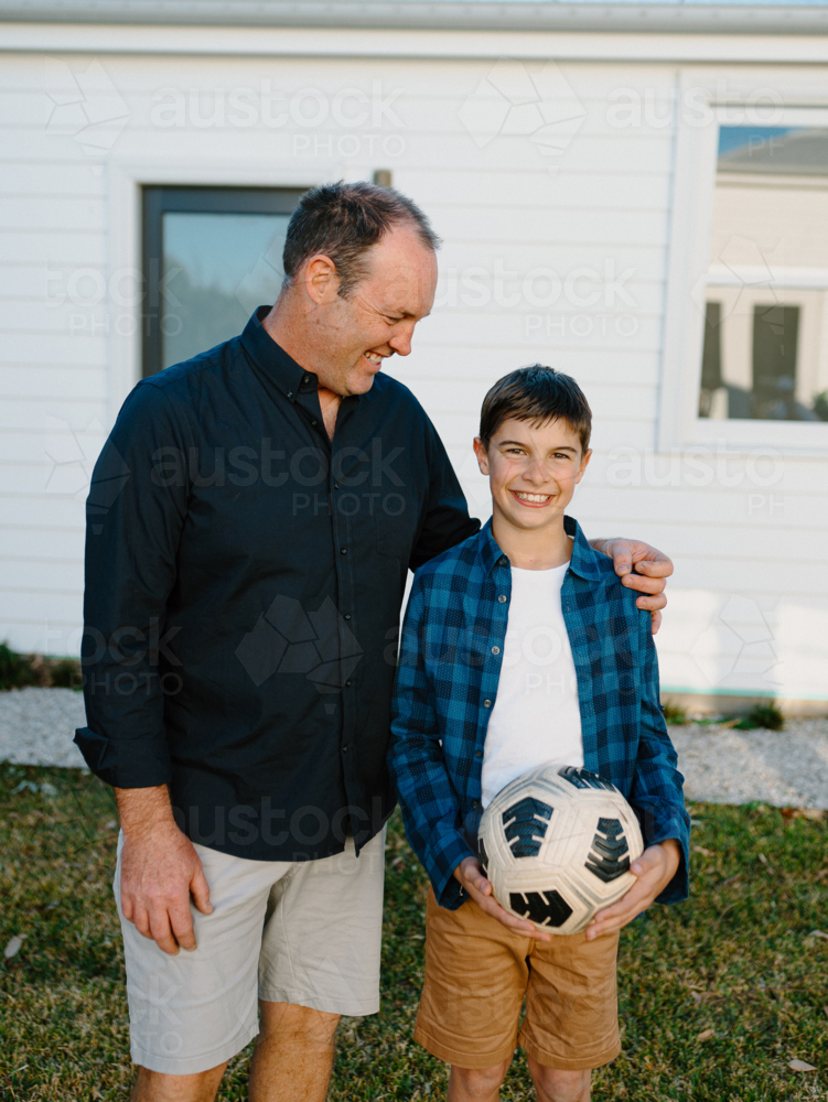 Father standing beside his son holding a soccer ball. - Australian Stock Image