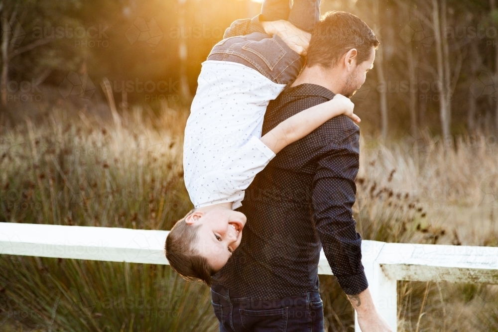 Father tipping son over his shoulder to carry him - Australian Stock Image