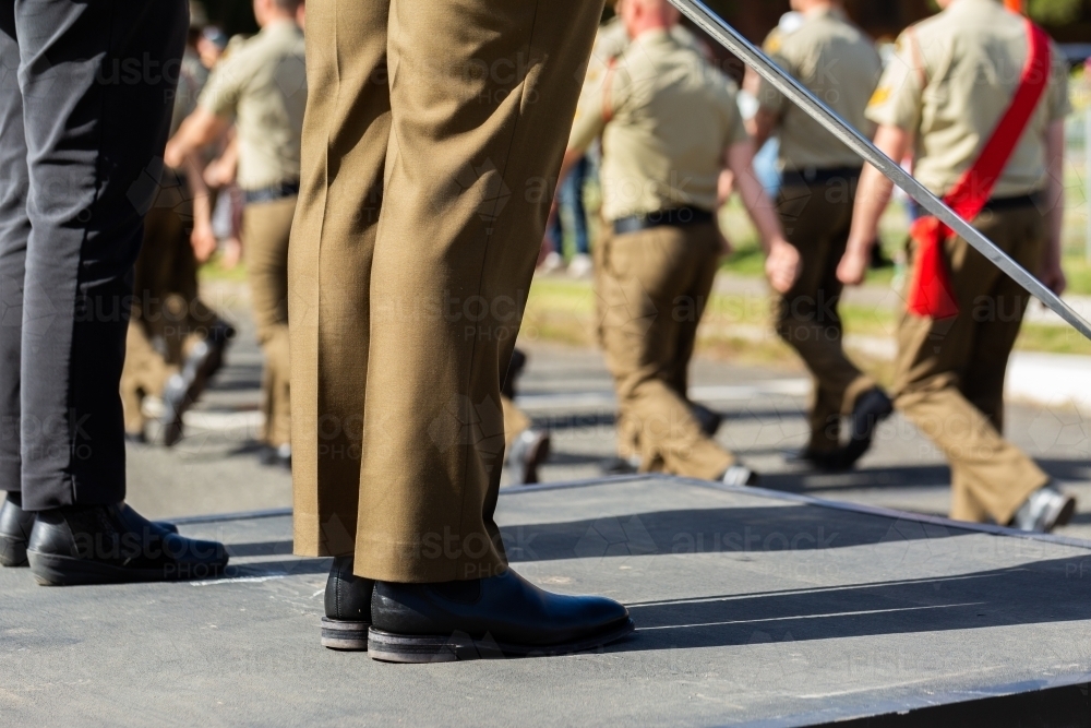 Feet of army officer holding sword standing with dignitary on platform with soldiers marching past - Australian Stock Image