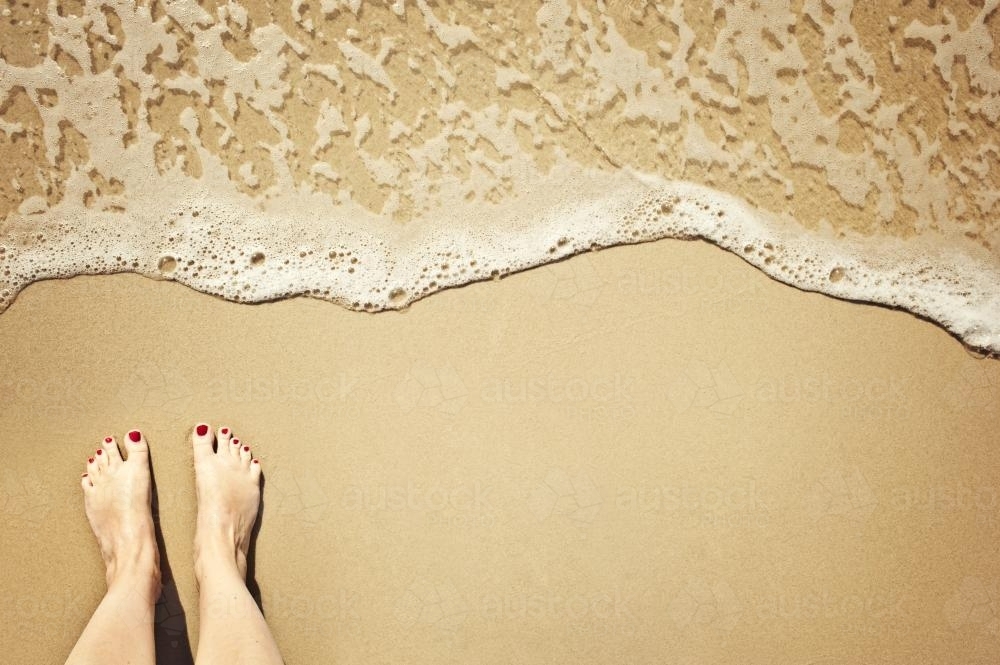 Feet on the sand as a wave approaches - Australian Stock Image