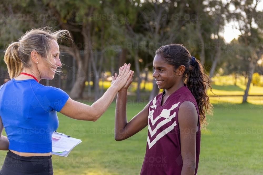 female coach high fives aboriginal student football player - Australian Stock Image