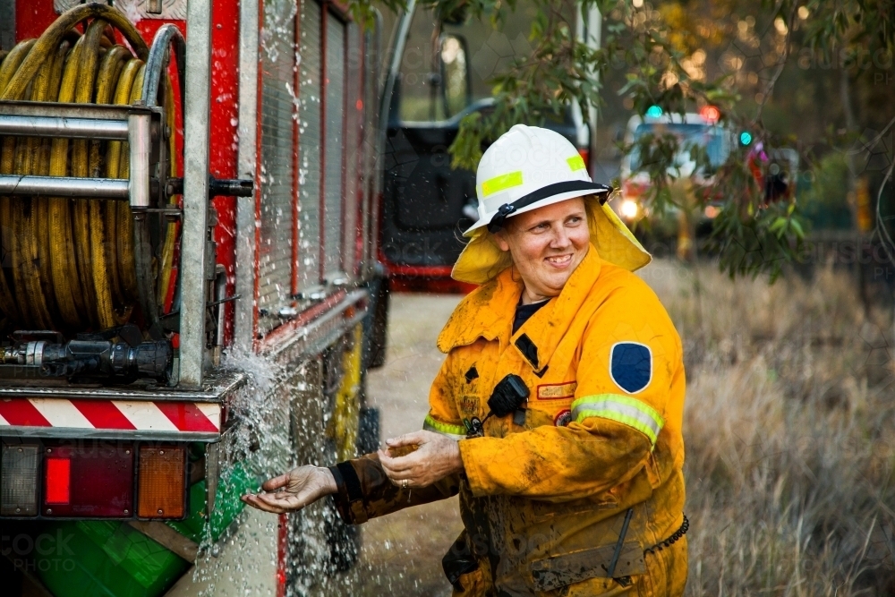 Female firefighter laughing and washing her hands beside firetruck - Australian Stock Image