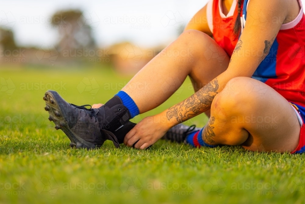 female football player sitting on grass adjusting ankle brace - Australian Stock Image