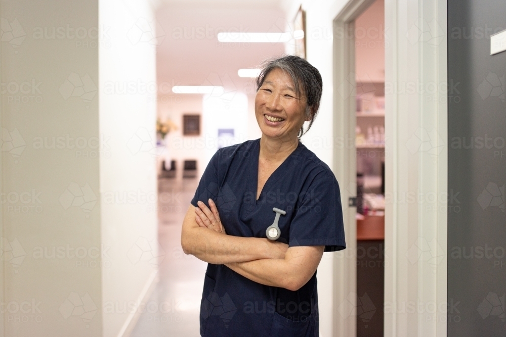 female middle aged healthcare worker with arms crossed smiling at the camera - Australian Stock Image