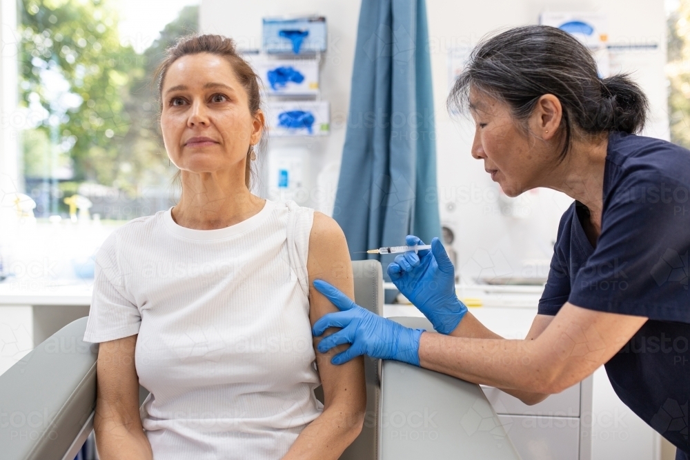 Female patient getting an injection on the arm by a female healthcare practitioner in a clinic - Australian Stock Image