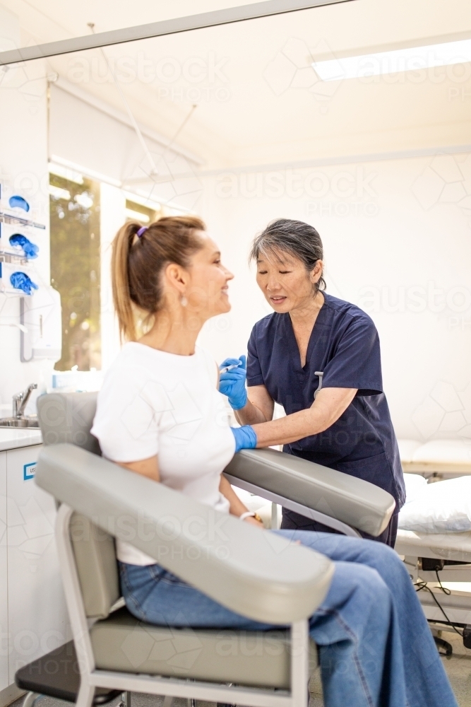 Female patient getting an injection on the arm by a female healthcare practitioner in a clinic - Australian Stock Image