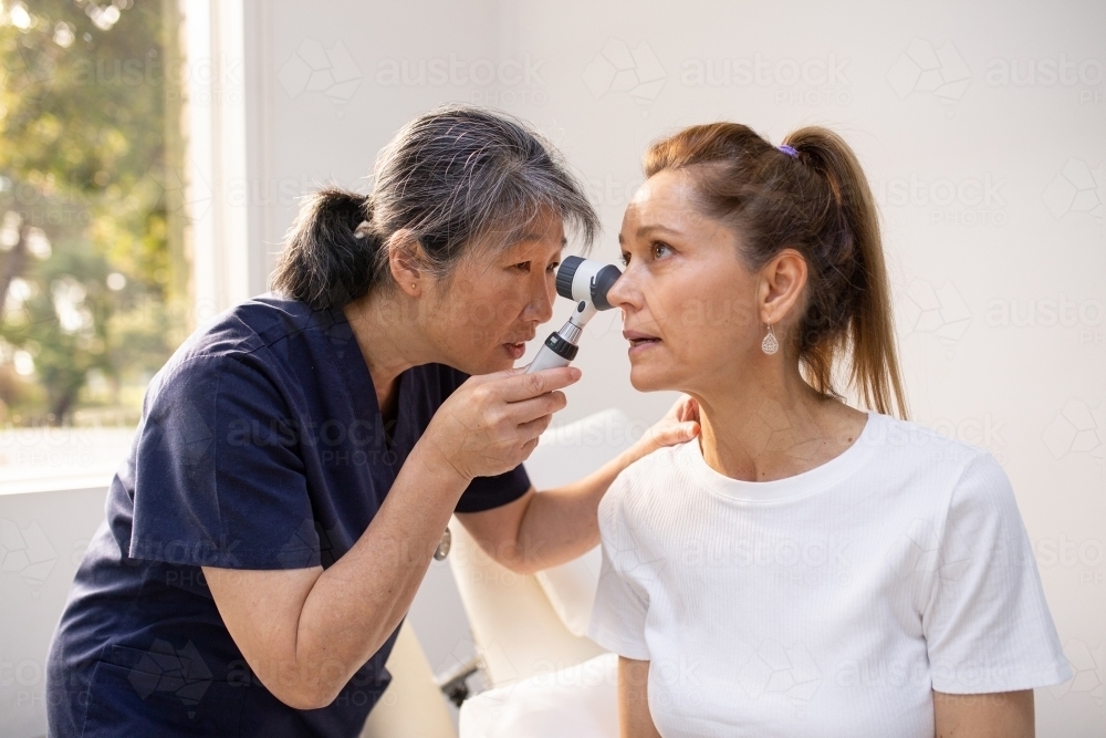 Female patient having her ears checked by a female nurse using an otoscope in the clinic - Australian Stock Image