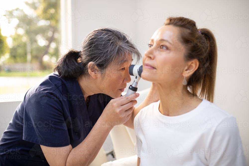 Female patient having her ears checked by a female nurse using an otoscope in the clinic - Australian Stock Image