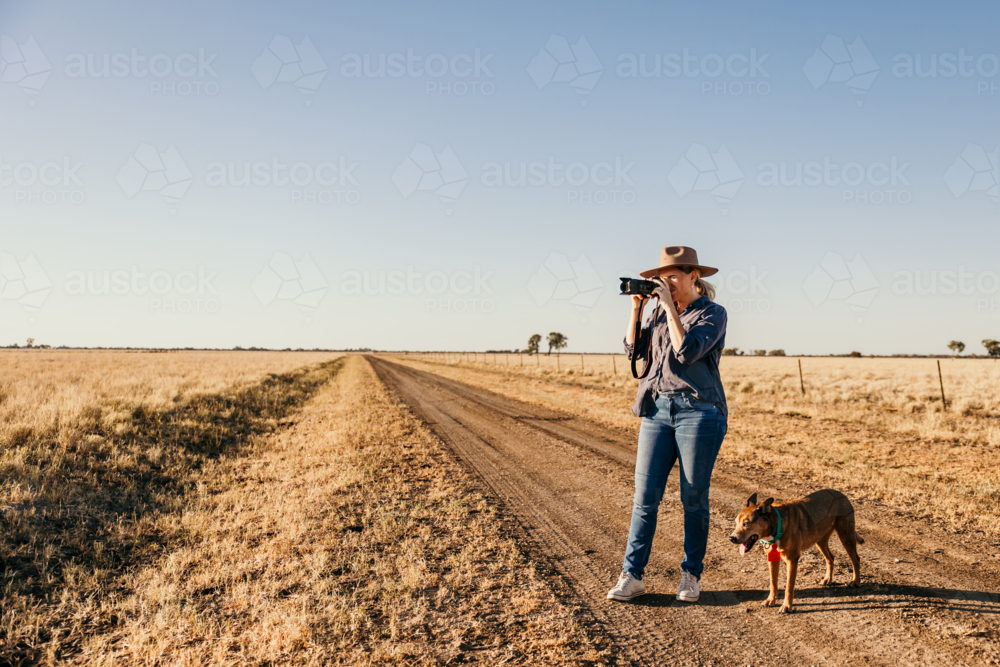 Female photographer looking through camera on farm with dog - Australian Stock Image