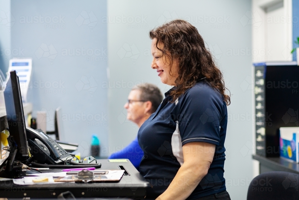 female receptionist working at stand up desk in physio clinic office - Australian Stock Image