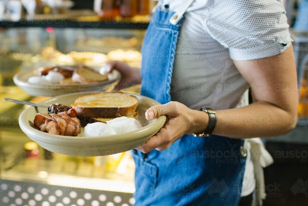 Female server serving two breakfast plates with toast, eggs, and bacon - Australian Stock Image