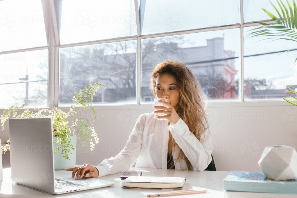 Female sipping water while working in a bright clinical white office - Australian Stock Image