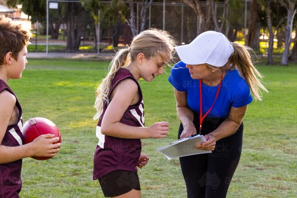 female sports coach interacting with young girl football player with clipboard - Australian Stock Image