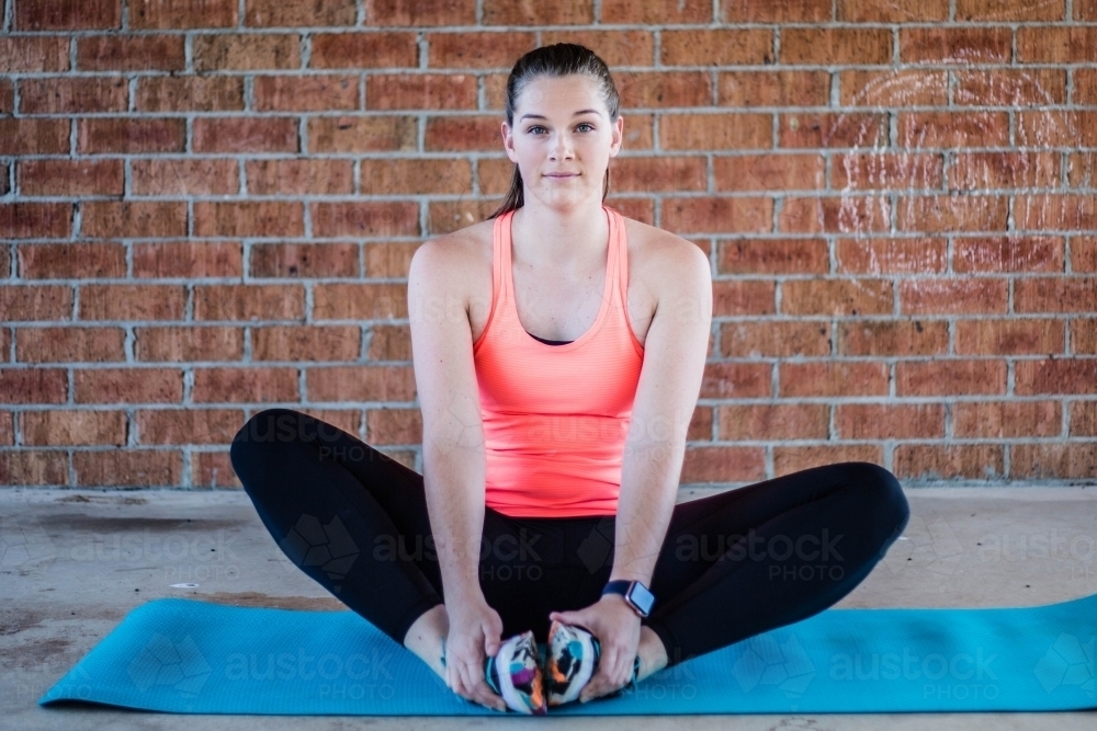 Female stretching on yoga mat with brick wall background - Australian Stock Image