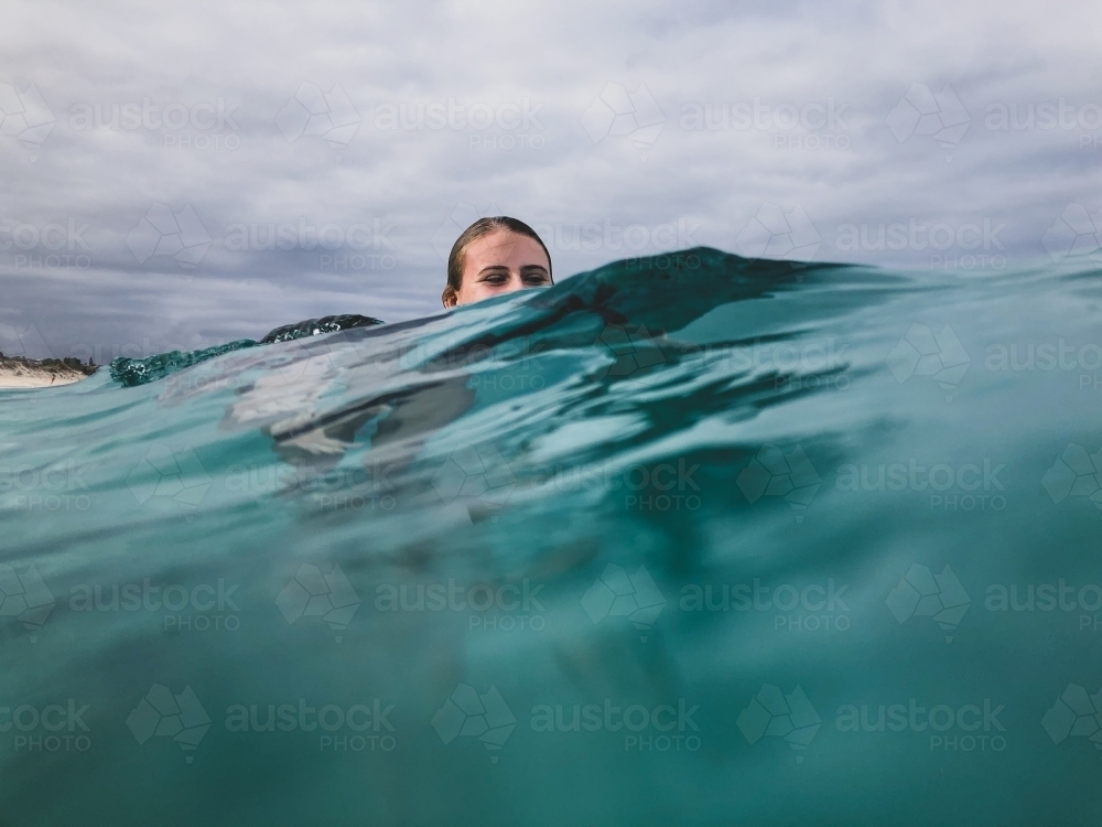 Female teenager with head semi submerged floating in ocean on glassy overcast day - Australian Stock Image