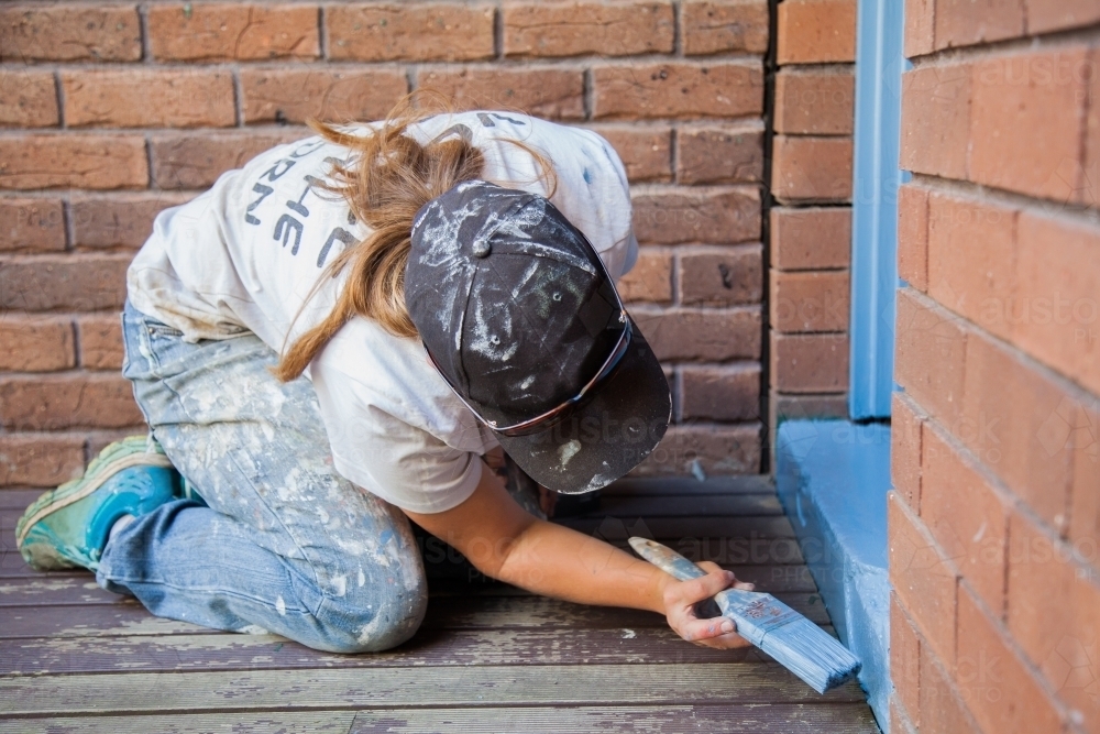 Female tradie painting back doorstep of home - Australian Stock Image