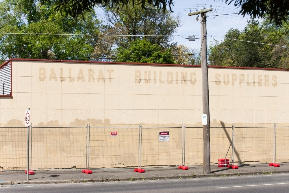 Fenced off wall of old building with faded signage - Australian Stock Image