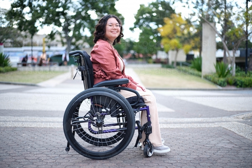 Filipina woman in wheelchair smiling at camera in park - Australian Stock Image