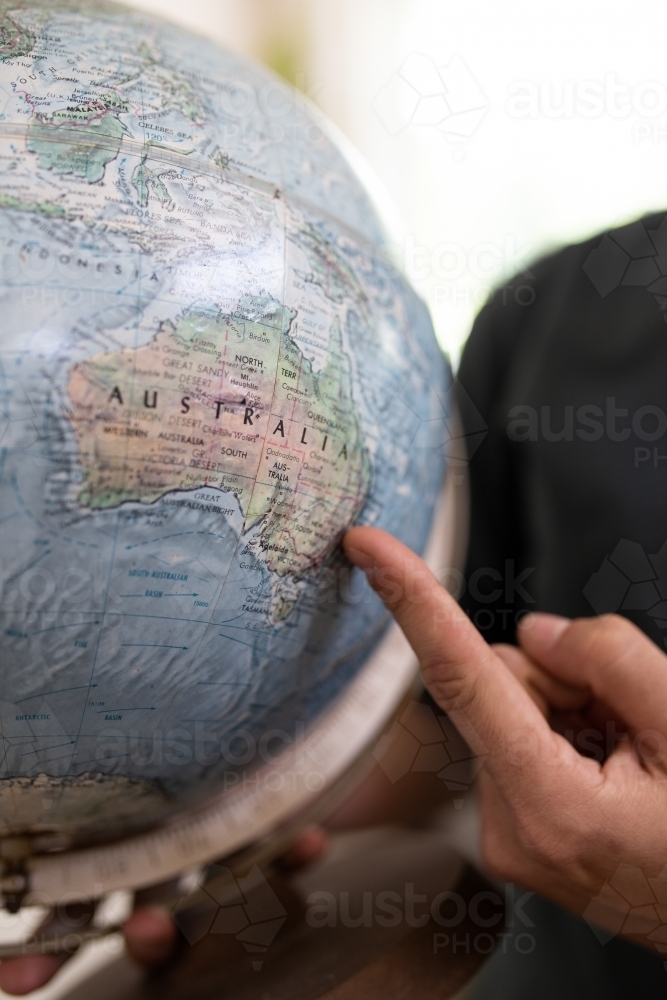 Finger pointing to map of Australia on round world globe - Australian Stock Image