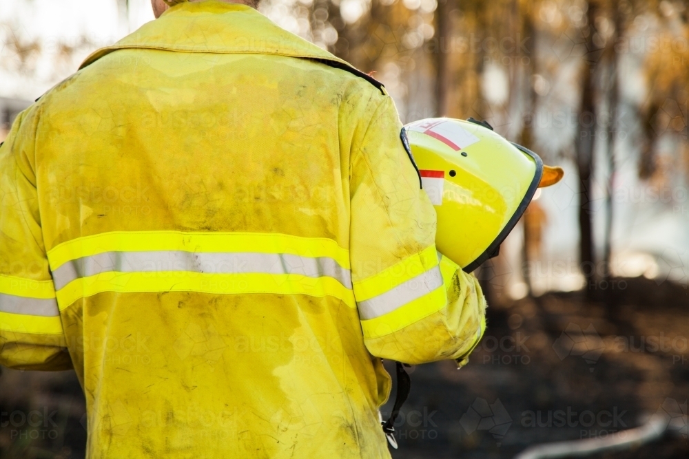 Fire fighter standing beside burnt grass area holding safety helmet in hand - Australian Stock Image