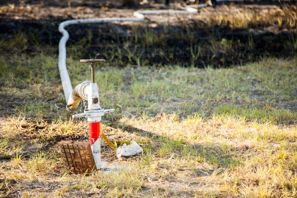 Fire hydrant beside burnt property with fire hose attached - Australian Stock Image