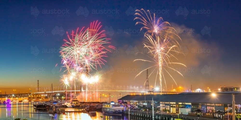 Fireworks going off in a twilight sky over a city marina. - Australian Stock Image