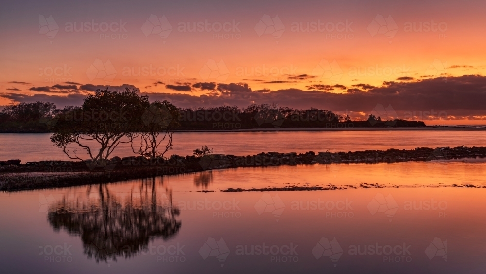 First Light/Sunrise looking across a tranquil river with silhouetted trees - Australian Stock Image