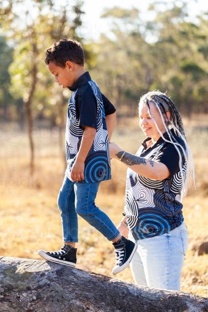 First nations Australian boy with mum walking on log in country paddock - Australian Stock Image