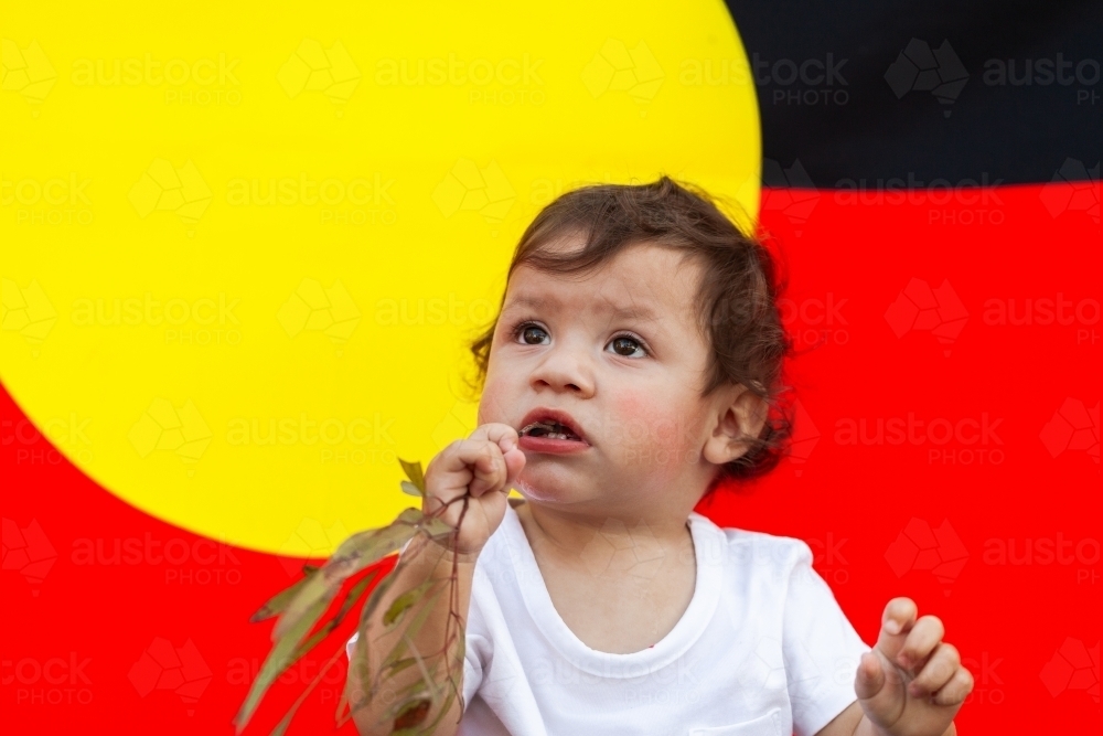 First Nations Australian child looking up against aboriginal flag backdrop - Australian Stock Image