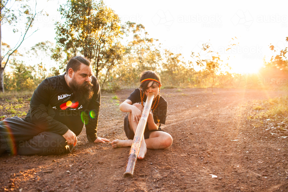 First Nations Australian father teaching Aboriginal son to play didgeridoo in rural Australia - Australian Stock Image