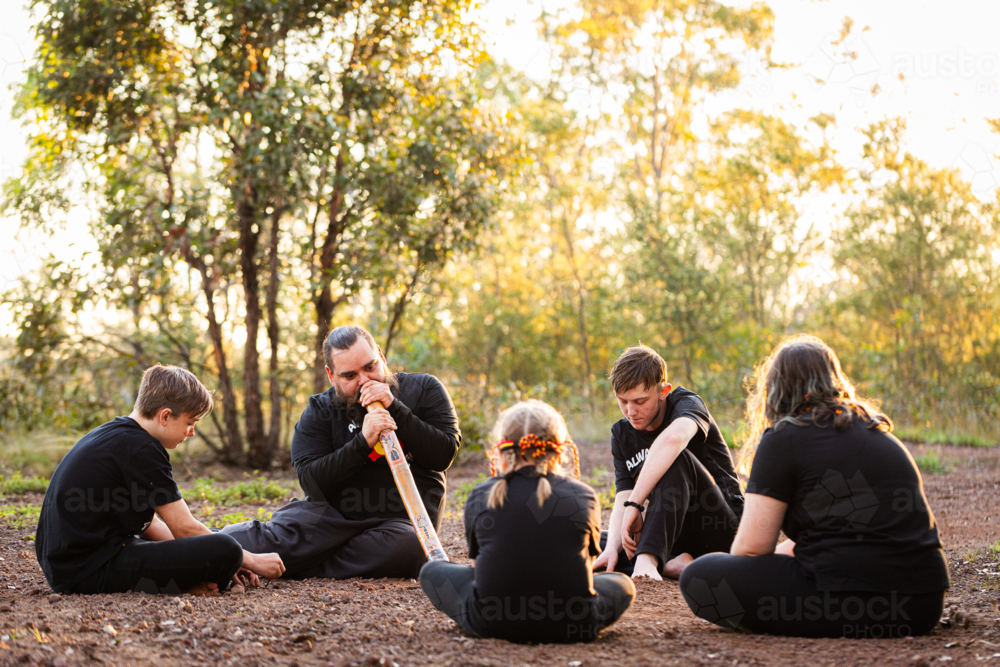 Image of First Nations Australian man with his kids sitting in bushland ...