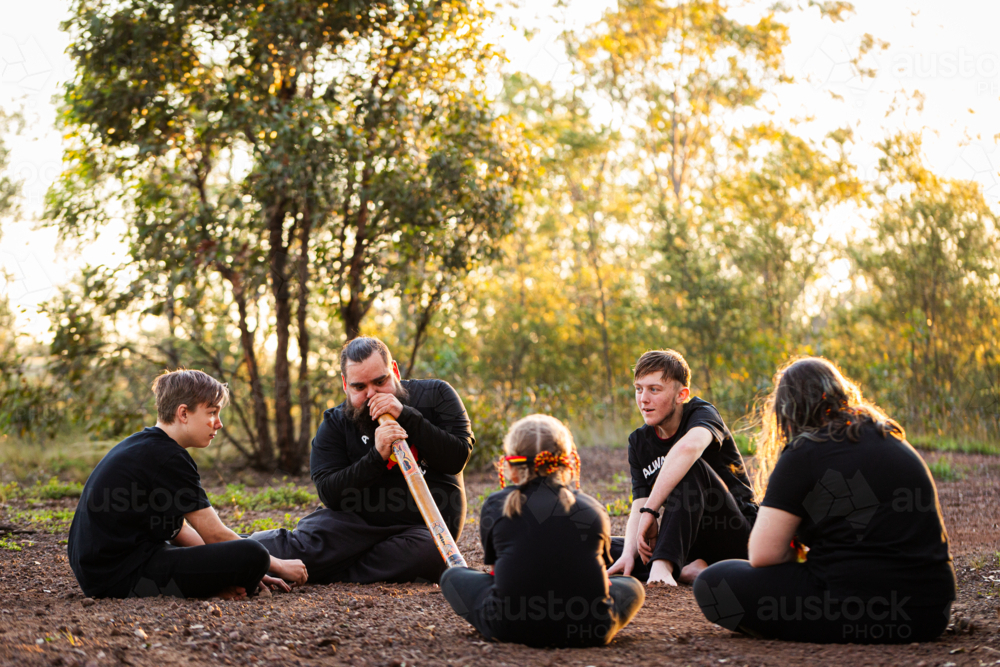 Image of First Nations Australian man with his kids sitting in bushland ...