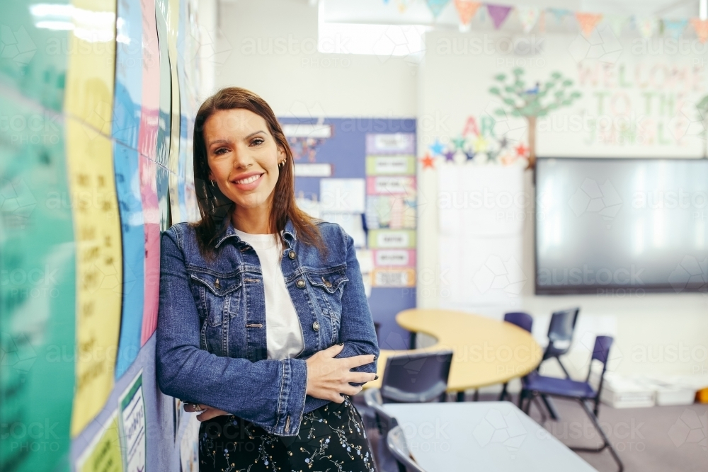 First Nations public school teacher leaning on the classroom wall smiling - Australian Stock Image
