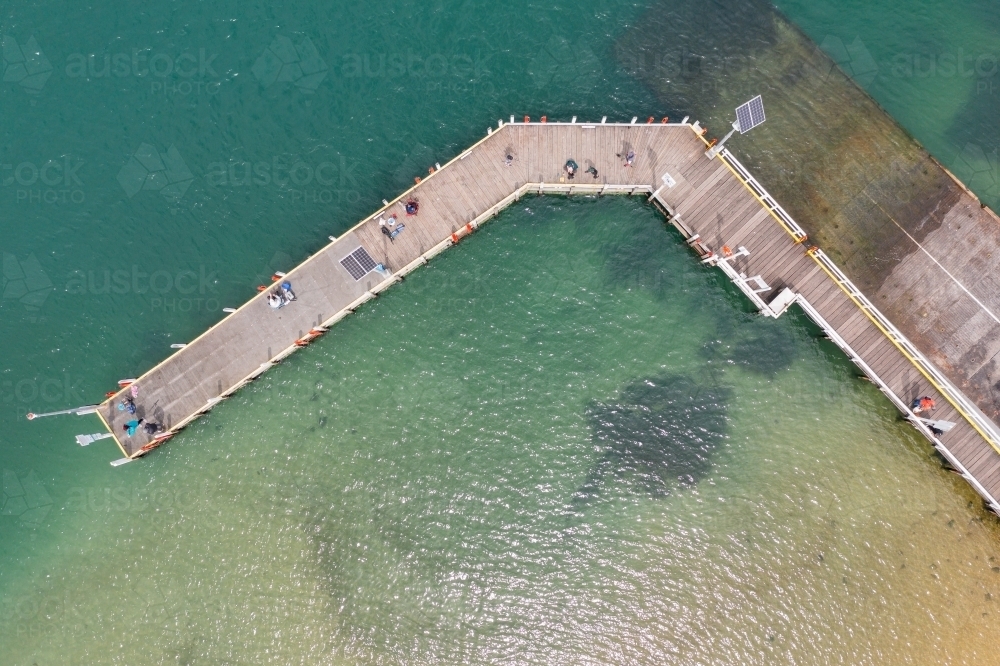 Fishermen and tourists on a wooden pier over a calm coastal bay - Australian Stock Image